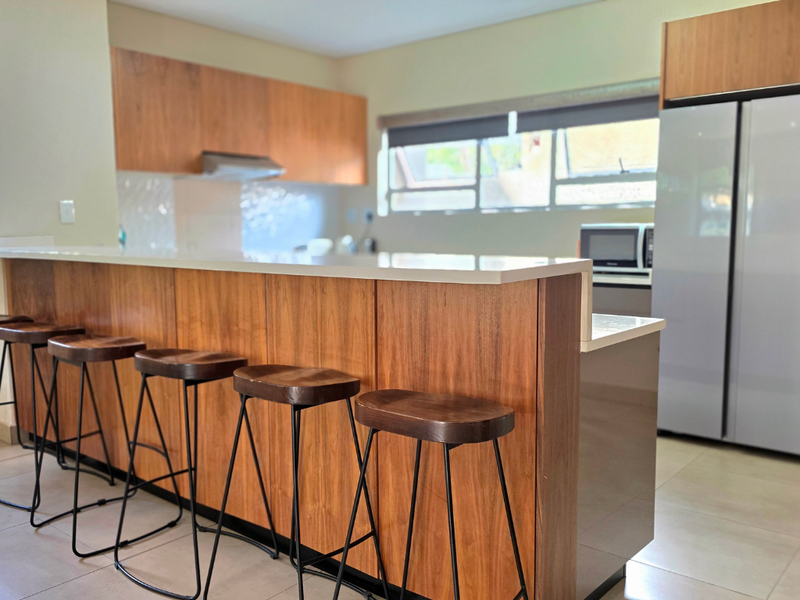 Modern kitchen featuring warm wood cabinetry, a spacious stone breakfast bar, and tiled flooring, offering a functional and contemporary cooking and dining space.