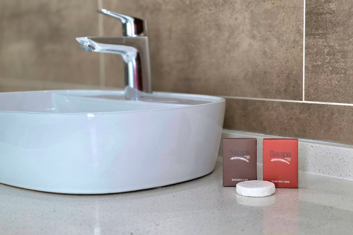 A close-up view of a modern bathroom vanity featuring a white vessel sink, chrome mixer tap, and neutral-toned ceramic wall tiles.