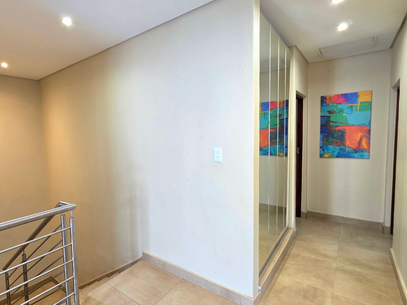 A bright, modern hallway featuring tiled flooring, recessed downlighting, and a sleek stainless steel balustrade overlooking the staircase.