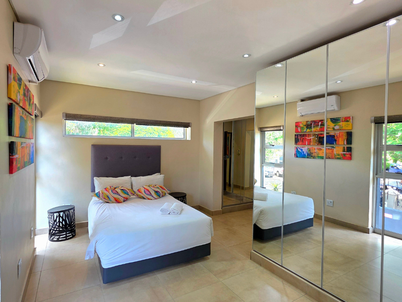 A modern bedroom featuring tiled flooring, recessed downlighting, a split-system air conditioner, and a large mirrored built-in wardrobe.