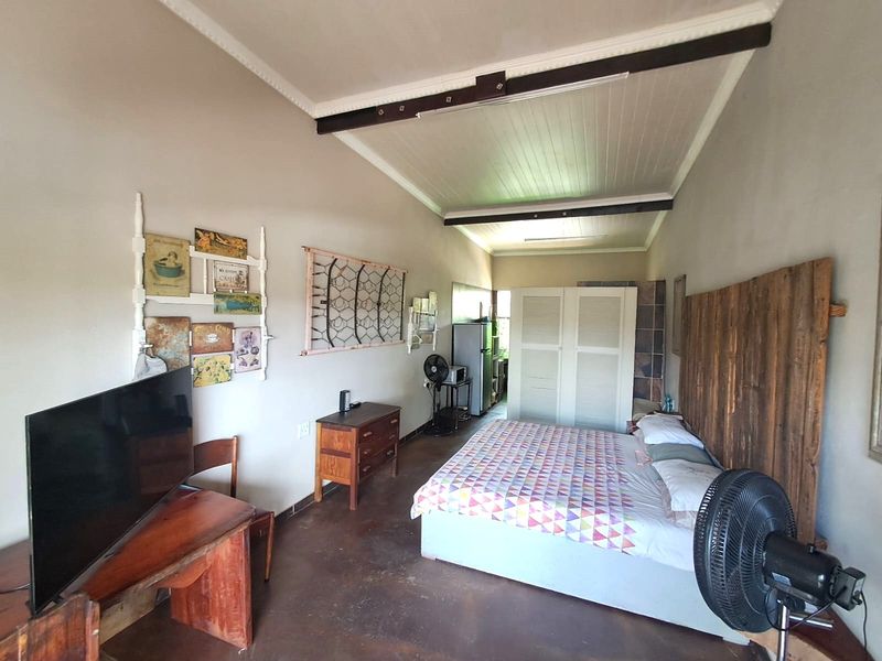 A bedroom featuring concrete flooring, timber ceiling beams, and a built-in wardrobe, offering a rustic aesthetic with potential for modern updates.