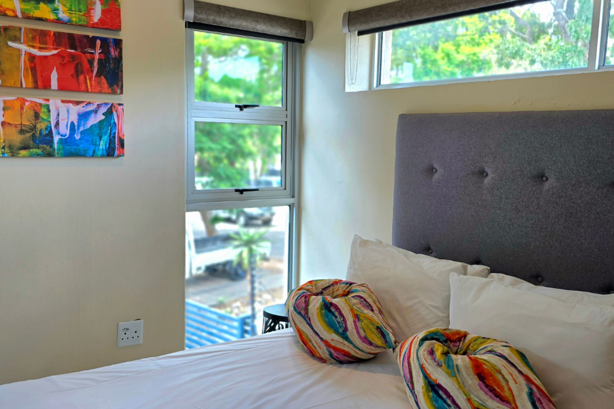 A bright bedroom featuring modern aluminium window frames, roller blinds, and neutral wall finishes, offering a comfortable and well-lit living space.