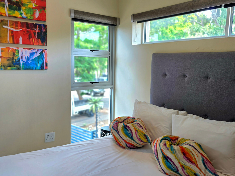 A bright bedroom featuring modern aluminium window frames, roller blinds, and neutral wall finishes, offering a comfortable and well-lit living space.