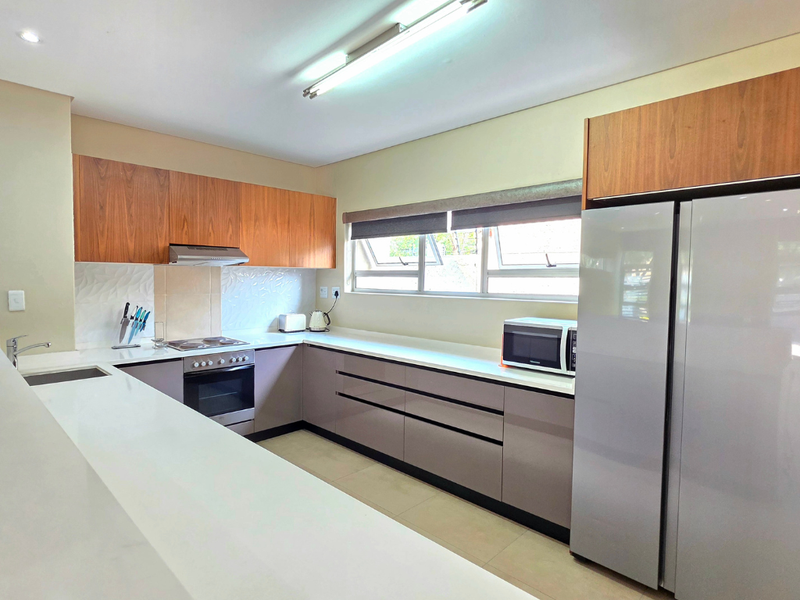 Modern kitchen featuring sleek cabinetry, stone countertops, integrated appliances, and ample workspace, illuminated by bright overhead lighting.