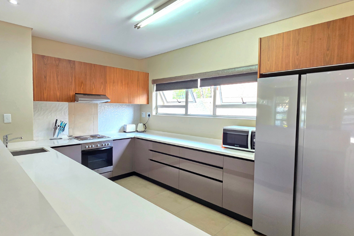 Modern kitchen featuring sleek cabinetry, stone countertops, integrated appliances, and ample workspace, illuminated by bright overhead lighting.
