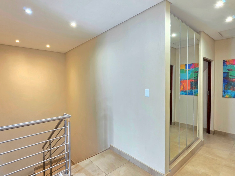 A bright, modern hallway featuring tiled flooring, a stainless steel balustrade, and a large mirrored built-in cupboard.