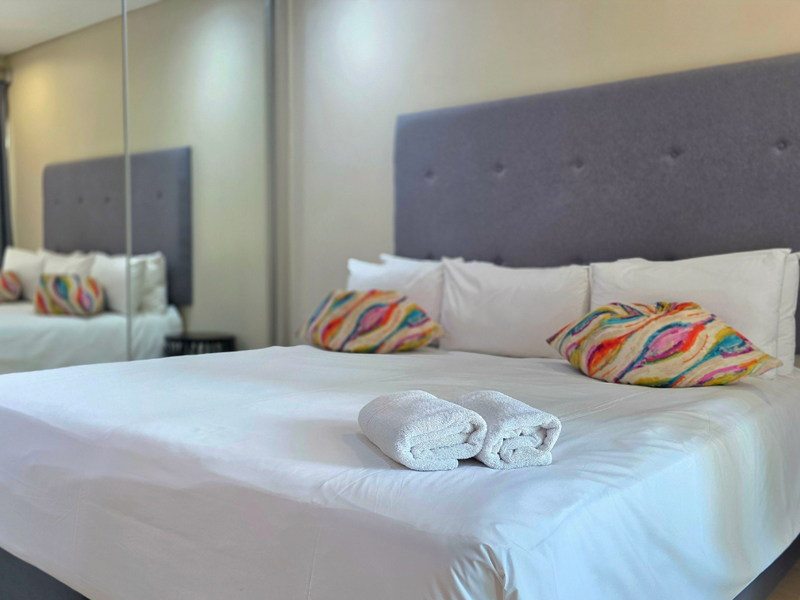 A well-maintained bedroom featuring a large bed and floor-to-ceiling mirrored sliding wardrobe doors, creating a bright and spacious atmosphere.