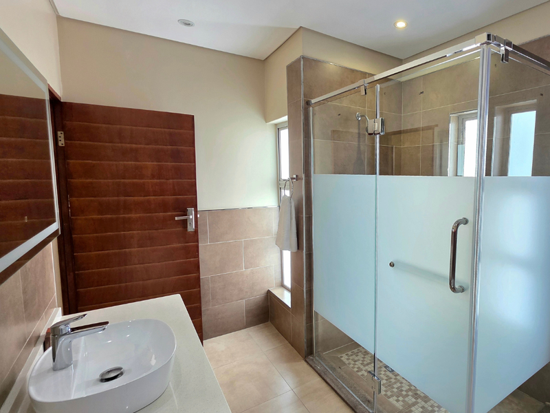 A modern bathroom featuring a vessel sink on a stone vanity, a glass-enclosed shower with frosted detailing, and neutral wall and floor tiling.