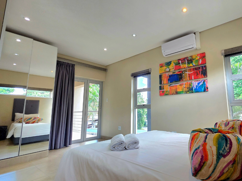 Modern bedroom featuring a mirrored built-in wardrobe, split-system air conditioning, tiled flooring, and direct access to a private balcony through sliding glass doors.
