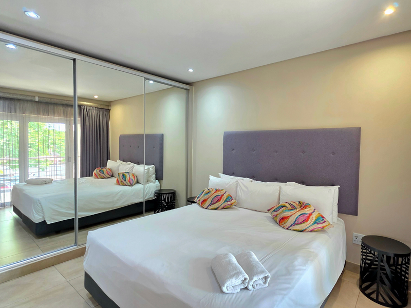 A well-maintained bedroom featuring large mirrored sliding wardrobes, recessed downlighting, and neutral tiled flooring, providing a clean and functional living space.