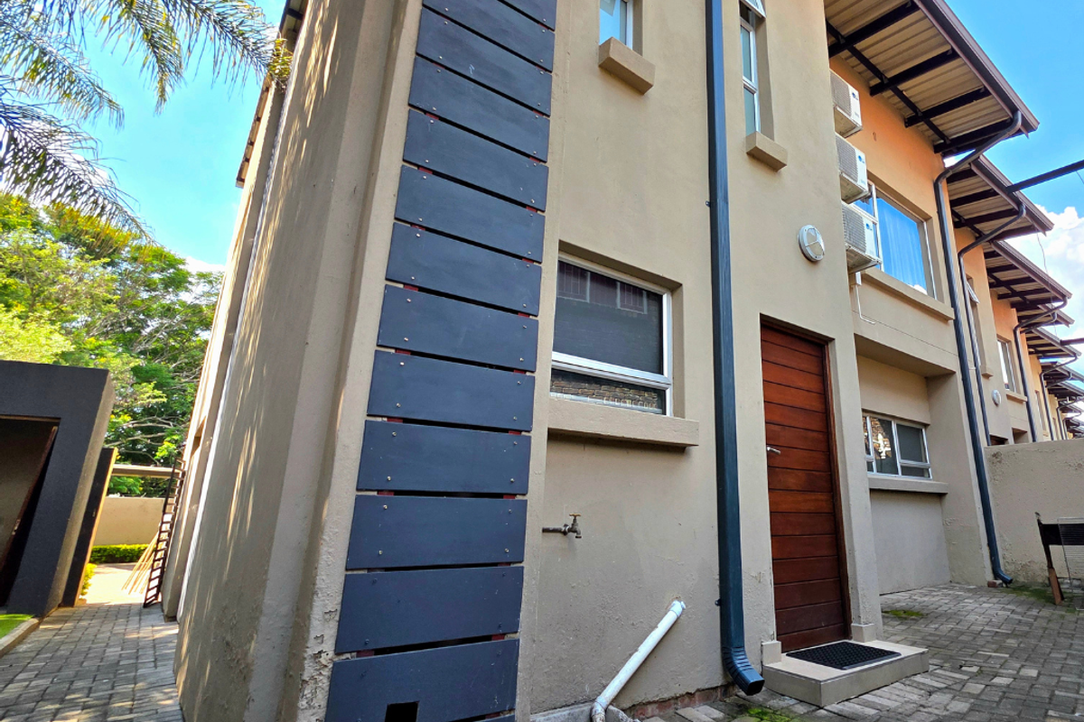 Rear exterior view of a townhouse featuring a timber door, paved courtyard, and wall-mounted air conditioning units.
