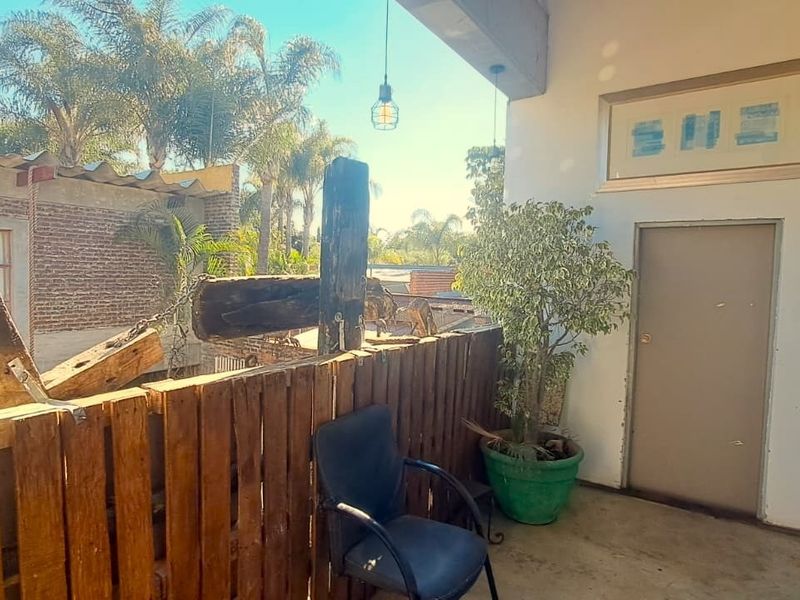A balcony area featuring a rustic wooden pallet railing, concrete flooring, and overhead pendant lighting, offering an outdoor space for relaxation.