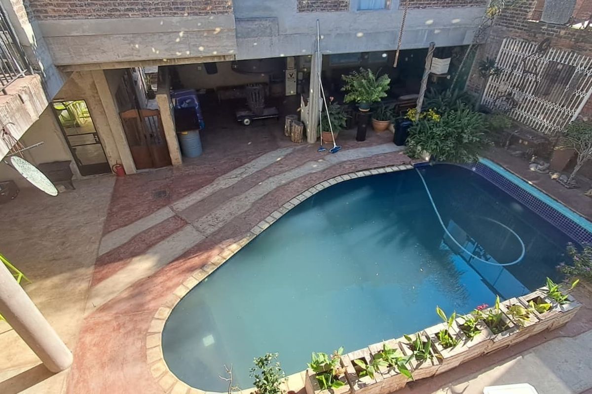 An elevated view of a private swimming pool area featuring a concrete patio, brick masonry walls, and an adjacent balcony.