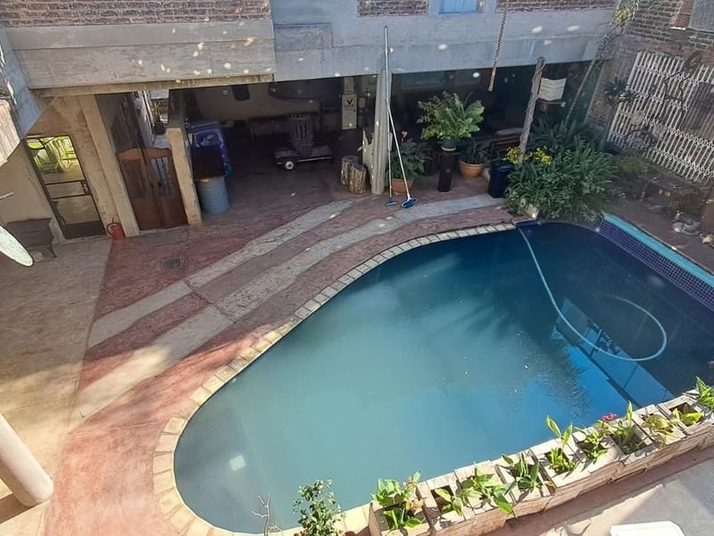 An elevated view of a private swimming pool area featuring a concrete patio, brick masonry walls, and an adjacent balcony.