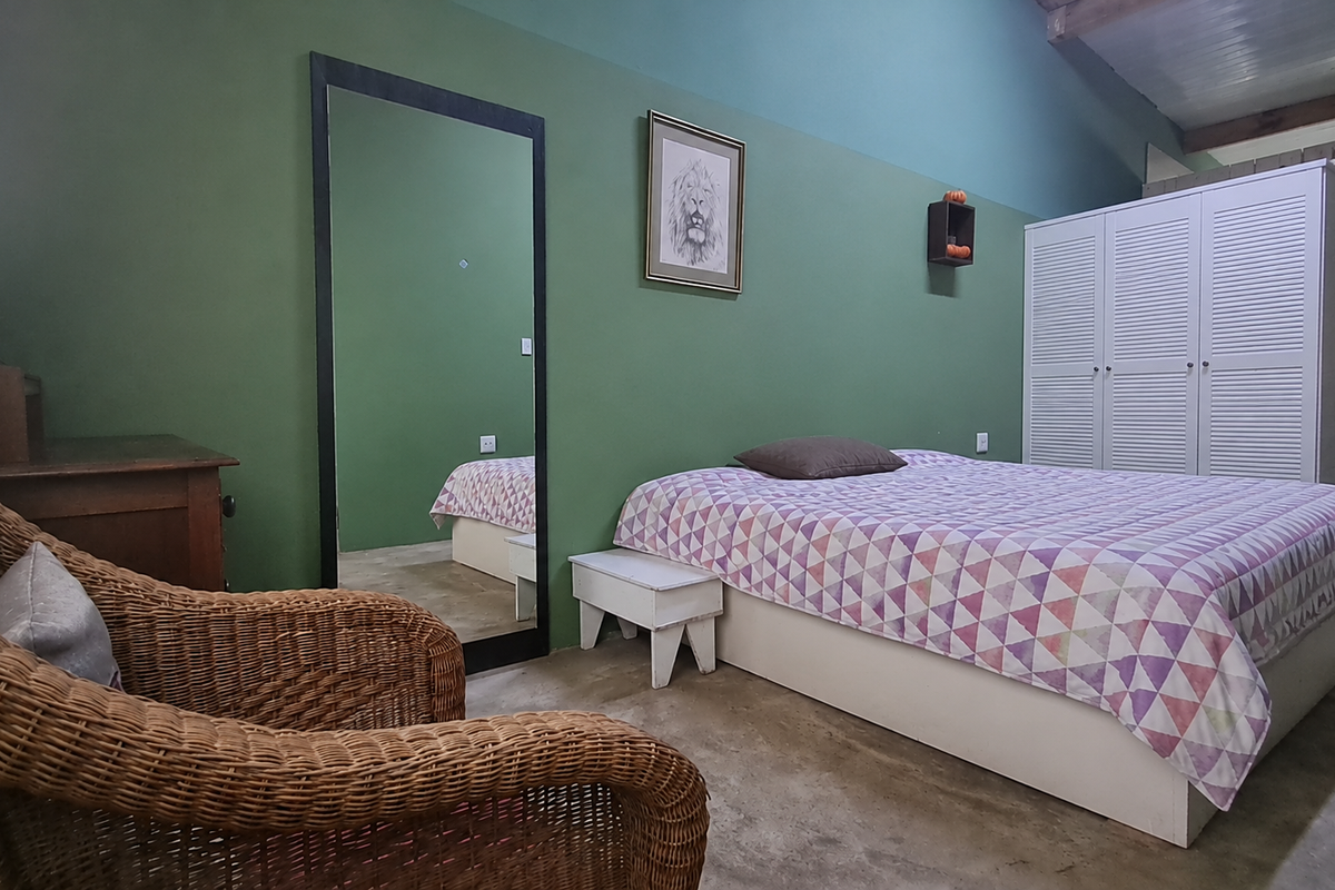 A bedroom featuring green painted walls, built-in white wardrobe cabinetry, and exposed ceiling beams, providing a rustic and functional living space.