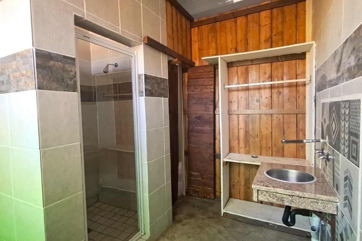 A bathroom featuring a shower enclosure, wall-mounted basin with granite vanity top, and a mix of tiled and timber wall finishes.