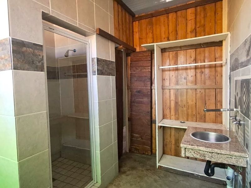 A bathroom featuring a shower enclosure, wall-mounted basin with granite vanity top, and a mix of tiled and timber wall finishes.