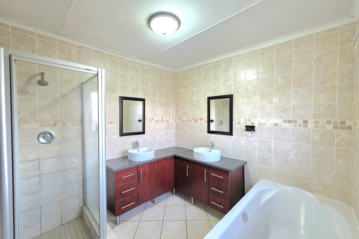 A spacious bathroom featuring a double vanity with vessel sinks, a separate shower enclosure, and a bathtub, finished with neutral wall and floor tiles.