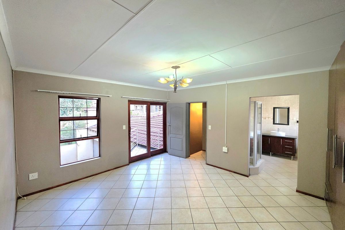 Spacious bedroom featuring tiled flooring, a sliding door to the exterior, and an open-plan en-suite bathroom with a vanity and shower.