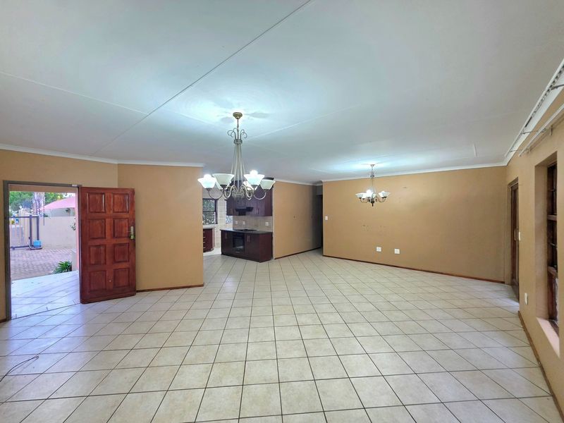 Spacious open-plan living and kitchen area featuring ceramic floor tiles, built-in cabinetry with integrated appliances, and dual chandeliers.