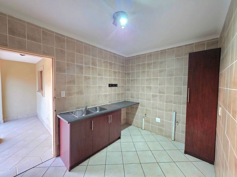 A functional laundry room featuring tiled walls and floors, a double basin sink with built-in cabinetry, and dedicated plumbing connections for appliances.