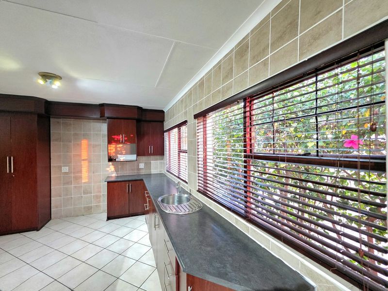 A functional kitchen featuring dark wood cabinetry, laminate countertops, a stainless steel sink, and neutral tiled backsplash and flooring.