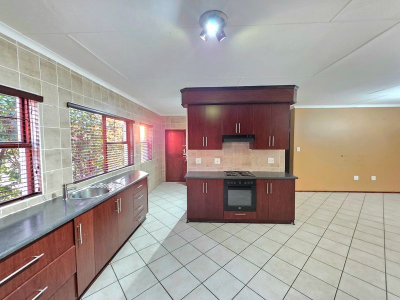 Spacious kitchen featuring dark wood cabinetry, laminate countertops, built-in oven and hob, tiled flooring, and a tiled backsplash.