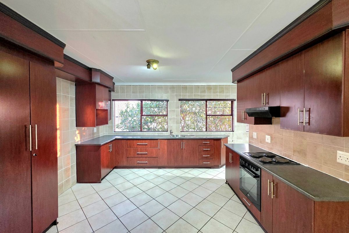 Spacious kitchen featuring dark wood cabinetry, laminate countertops, built-in oven, electric hob, extractor fan, and tiled flooring.