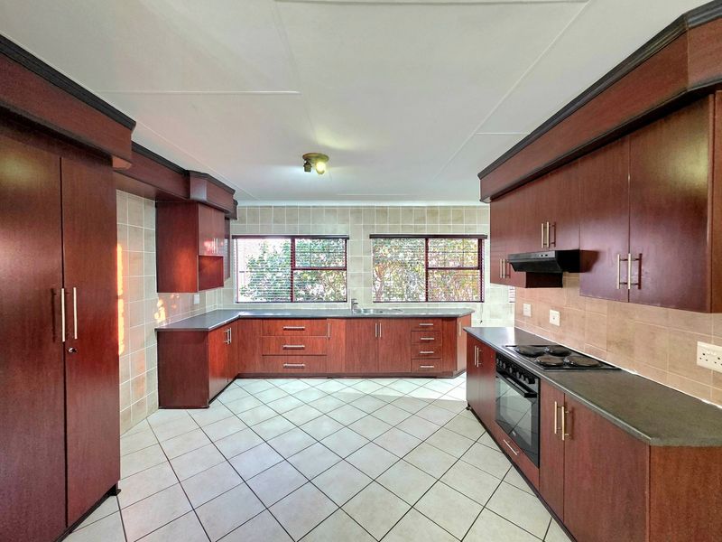 Spacious kitchen featuring dark wood cabinetry, laminate countertops, built-in oven, electric hob, extractor fan, and tiled flooring.