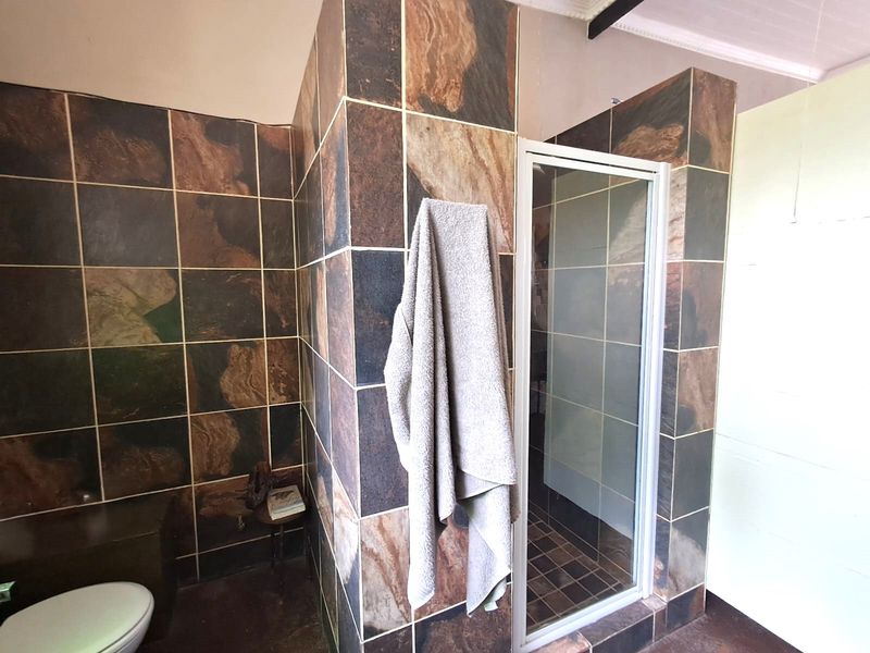 Bathroom featuring a shower enclosure with dark decorative wall tiles and a standard toilet.