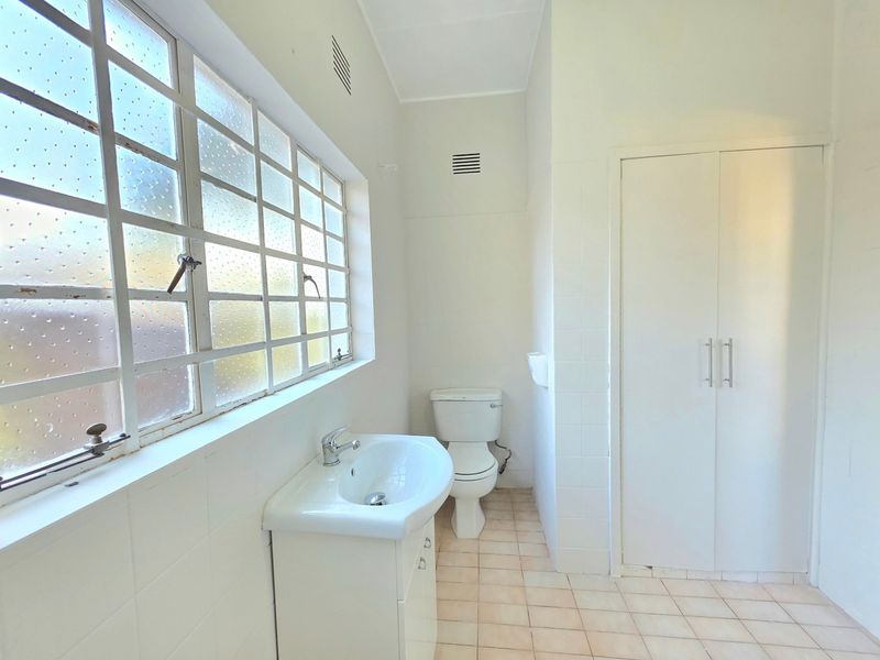A functional bathroom featuring a vanity basin, toilet, built-in storage cupboard, and tiled finishes, offering a clean and neutral space.