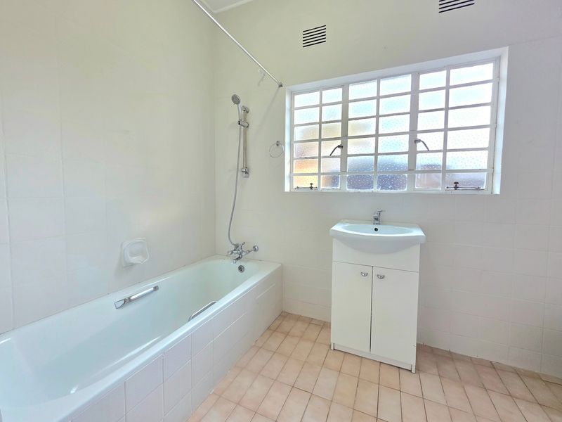 A functional bathroom featuring a bathtub with shower mixer, a vanity cabinet with washbasin, and tiled finishes throughout.