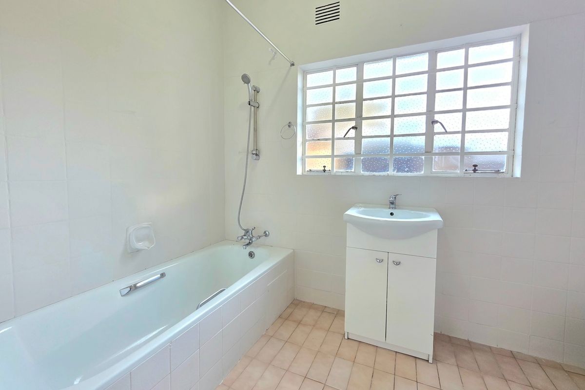A functional bathroom featuring a bathtub with shower mixer, a vanity cabinet with washbasin, and tiled finishes throughout.