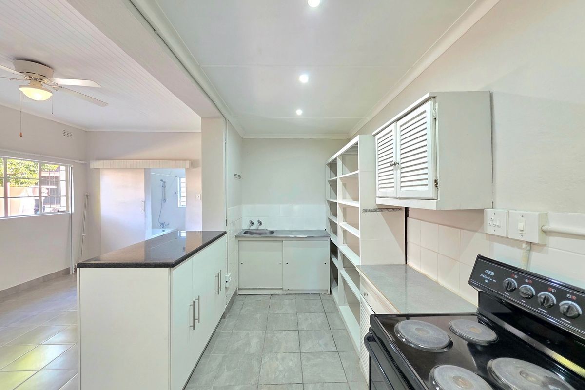 A functional kitchen featuring built-in cabinetry, granite countertops, a stainless steel sink, and a freestanding stove, with an open-plan layout leading to the living area.