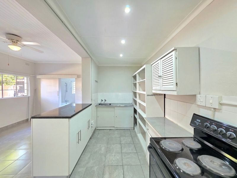 A functional kitchen featuring built-in cabinetry, granite countertops, a stainless steel sink, and a freestanding stove, with an open-plan layout leading to the living area.