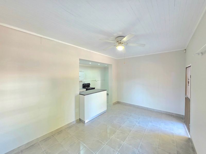 An open-plan living area featuring tiled flooring, a ceiling fan, and a breakfast counter leading into a kitchen space.