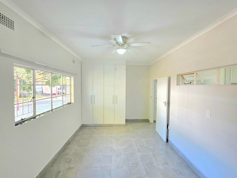 A bright, empty bedroom featuring neutral tiled flooring, built-in cupboards, and a ceiling fan, offering a clean and versatile space.
