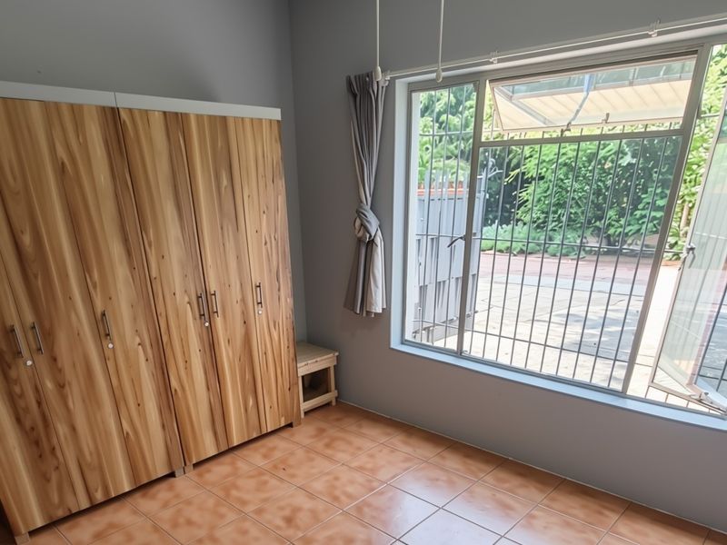 A bedroom featuring built-in wooden cupboards, tiled flooring, and a large window with security bars overlooking the exterior.
