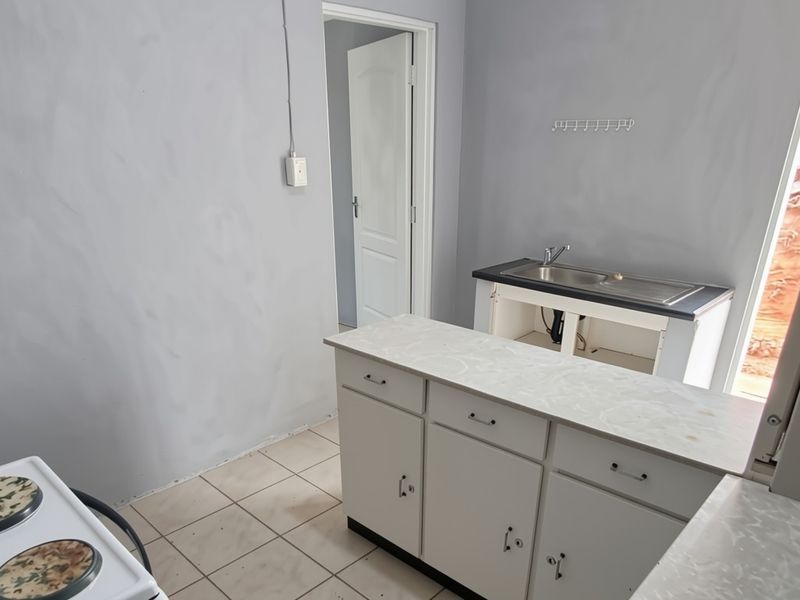 A compact kitchen area featuring tiled flooring, basic cabinetry, and a stainless steel sink, currently awaiting renovation or completion.