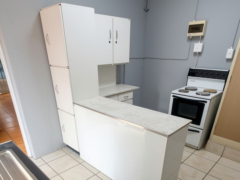 A functional kitchen area featuring white built-in cabinetry, a laminate countertop, and a freestanding stove, finished with ceramic floor tiles.