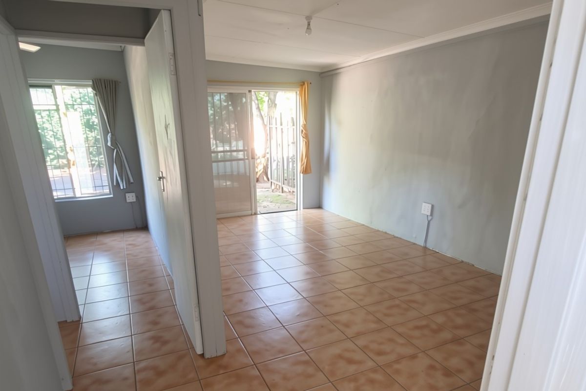 An empty, open-plan living area featuring tiled flooring, neutral walls, and direct access to an outdoor space through a sliding glass door.