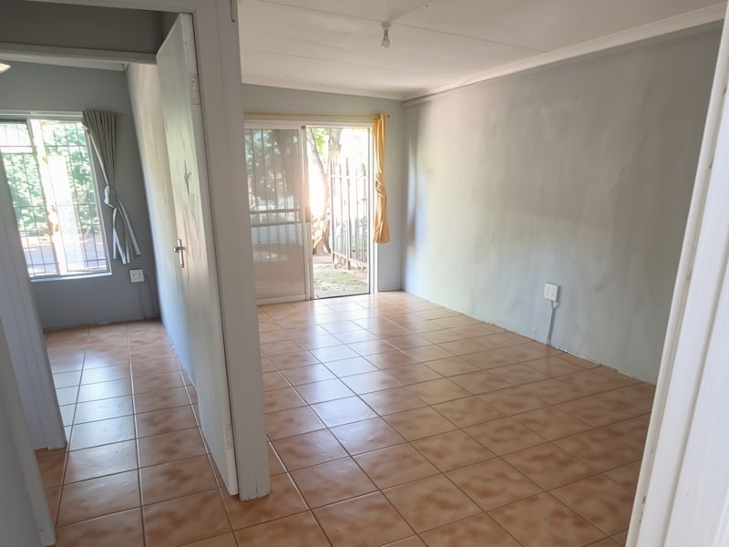 An empty, open-plan living area featuring tiled flooring, neutral walls, and direct access to an outdoor space through a sliding glass door.