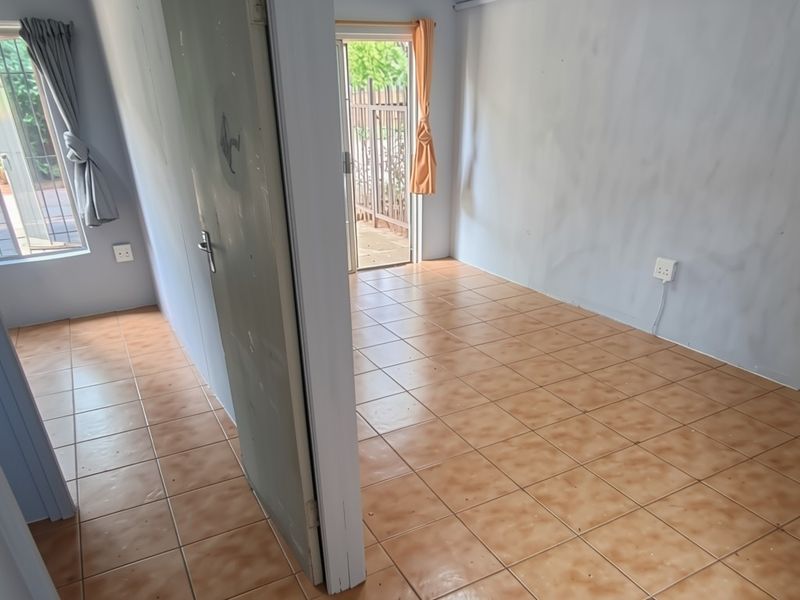 An empty living area featuring tiled flooring, neutral walls, and direct access to an outdoor space through a sliding door.
