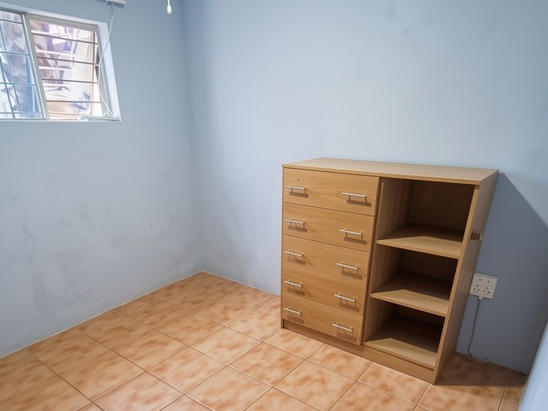 A bedroom featuring tiled flooring and a window with security bars, currently showing signs of wear on the wall surfaces.