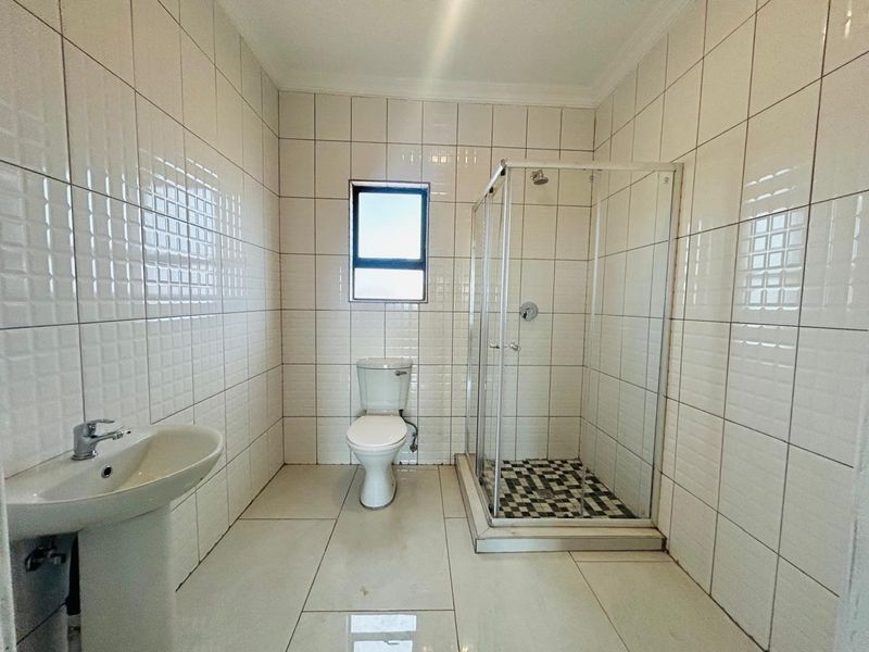 A clean, functional bathroom featuring a pedestal basin, a standard toilet, and a glass-enclosed shower with tiled finishes throughout.