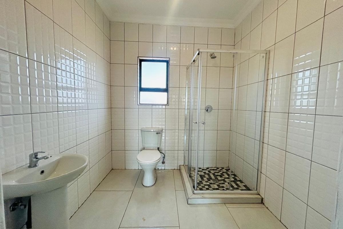 A clean, functional bathroom featuring a pedestal basin, a standard toilet, and a glass-enclosed shower with tiled finishes throughout.