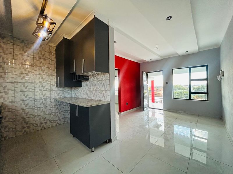 An open-plan living and kitchen area featuring modern dark cabinetry, granite countertops, polished tiled flooring, and access to a balcony.