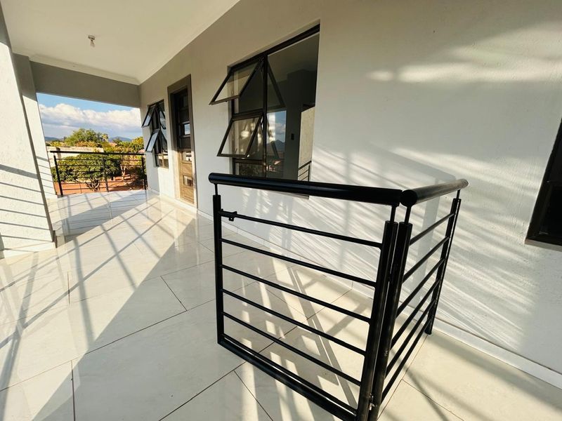 A spacious covered balcony featuring modern tiled flooring, a black metal balustrade, and top-hung windows, offering a clean and well-maintained outdoor living space.