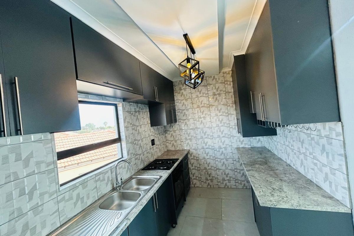 Modern galley-style kitchen featuring dark cabinetry, stone-look countertops, a gas hob, and a double stainless steel sink with tiled splashbacks.