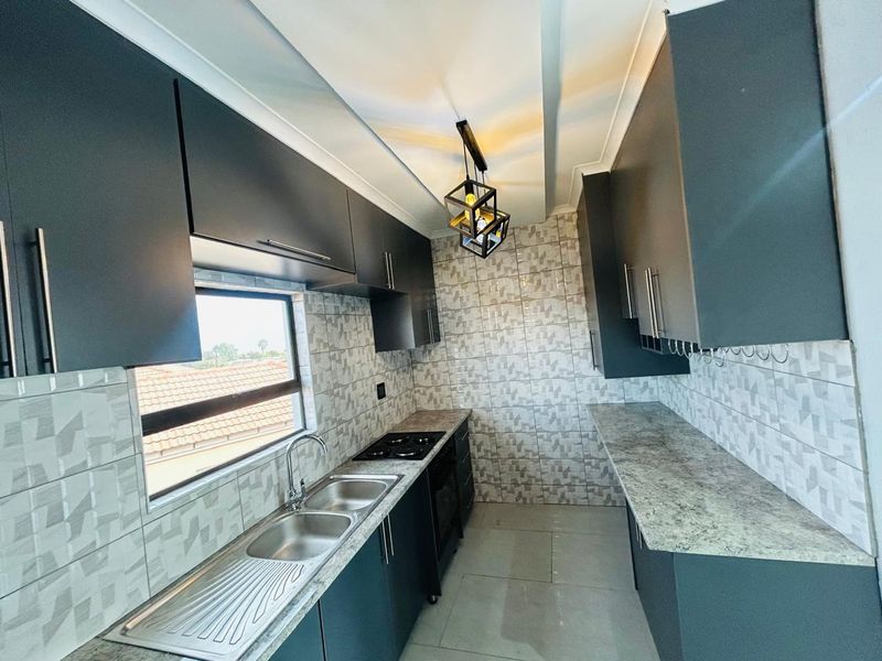 Modern galley-style kitchen featuring dark cabinetry, stone-look countertops, a gas hob, and a double stainless steel sink with tiled splashbacks.